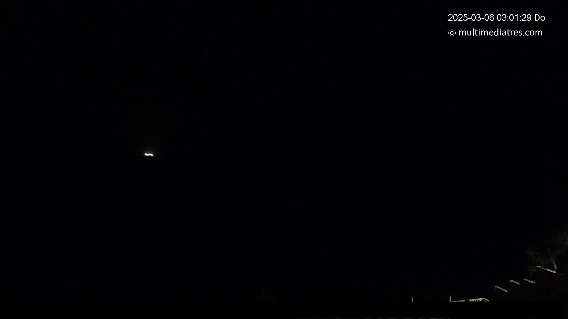 A faint light is visible in a dark night sky above a shadowy, low-lying structure.