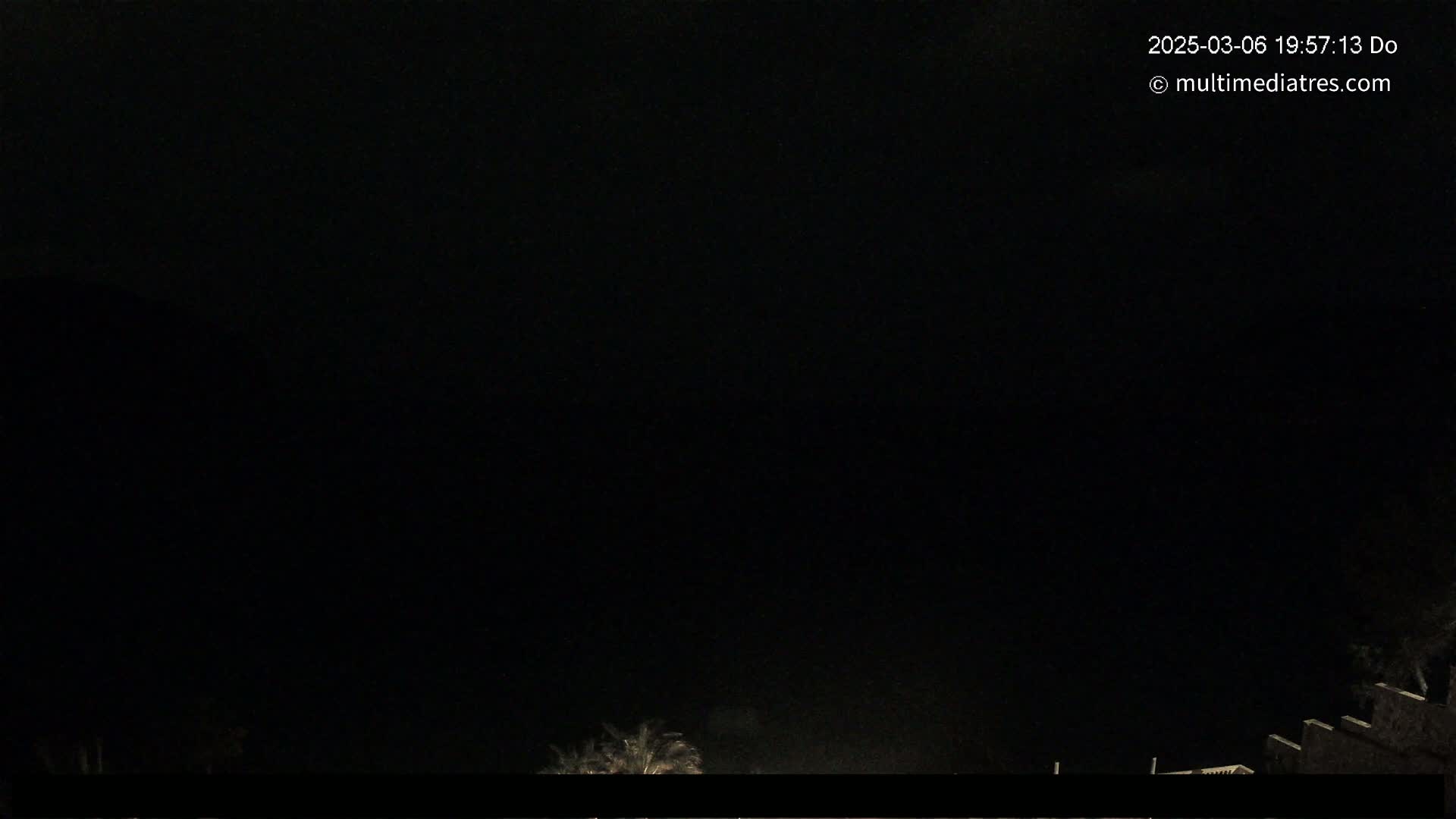 A nighttime, dark image shows the tops of some trees and a building at the bottom edge.