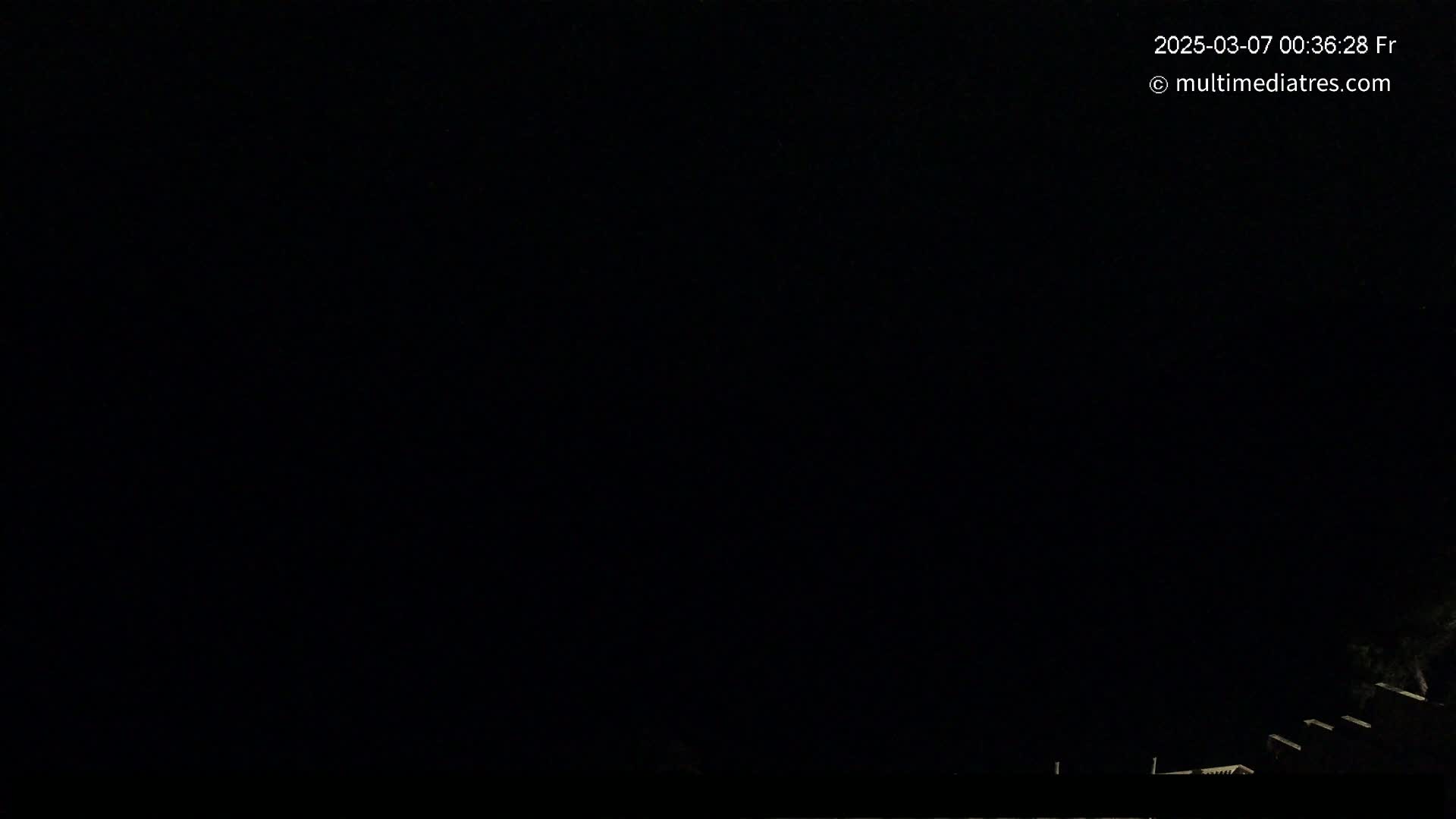 The image shows a dark, nighttime scene with a few dimly lit structures visible at the bottom edge.