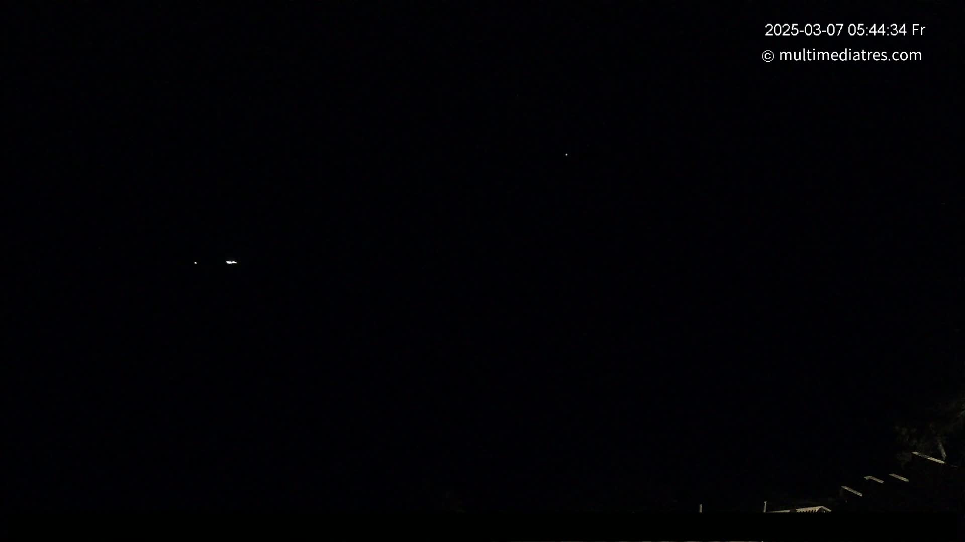 A dark night sky shows a few distant lights, and the silhouettes of buildings and trees are visible at the bottom.