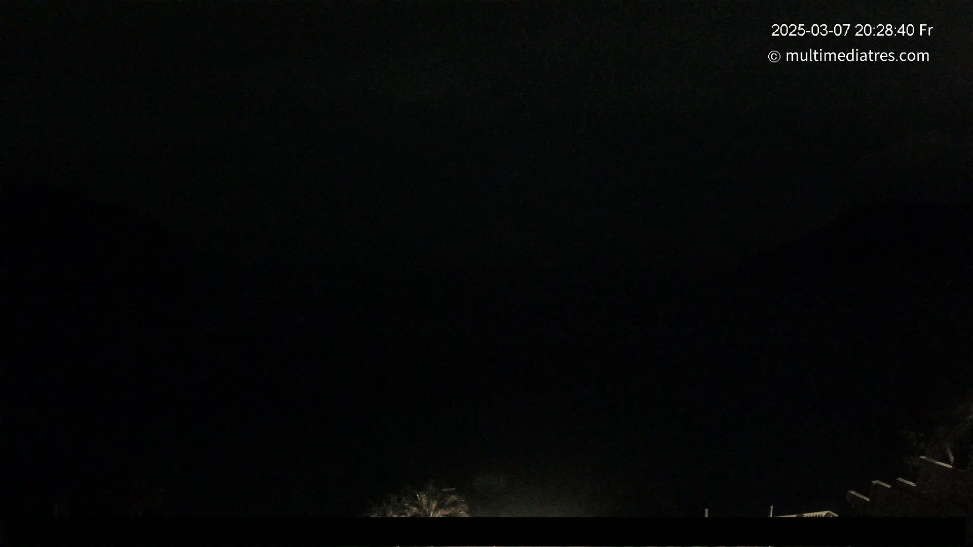 A nighttime outdoor scene shows a dark sky and the faint silhouettes of vegetation and structures at the bottom of the frame.