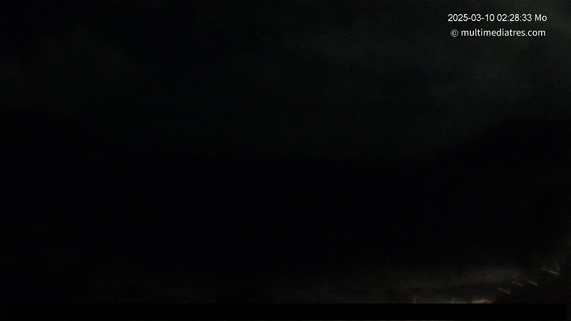 A dark, nighttime scene shows a mostly black sky with a very faint, hazy light near the bottom.