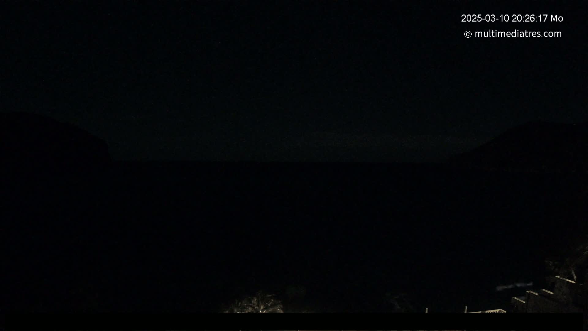 A nighttime view of a dark body of water between two silhouetted hills under a clear, dark sky.