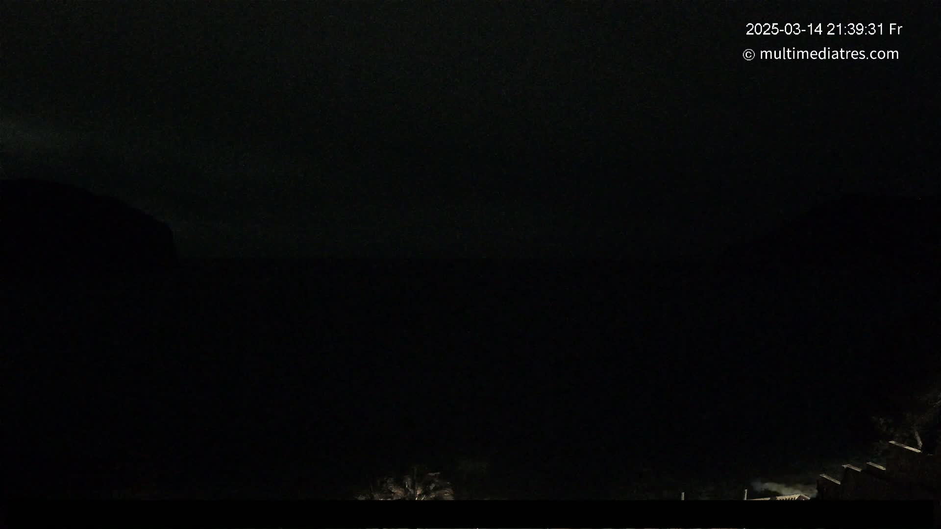 A dark, nighttime scene shows a mostly black sky with a few indistinct shapes of trees and buildings visible at the bottom.
