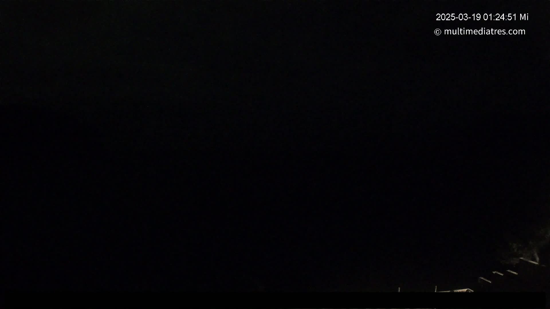 A dark nighttime scene shows a few dimly lit structures at the bottom of the frame under a completely black sky.