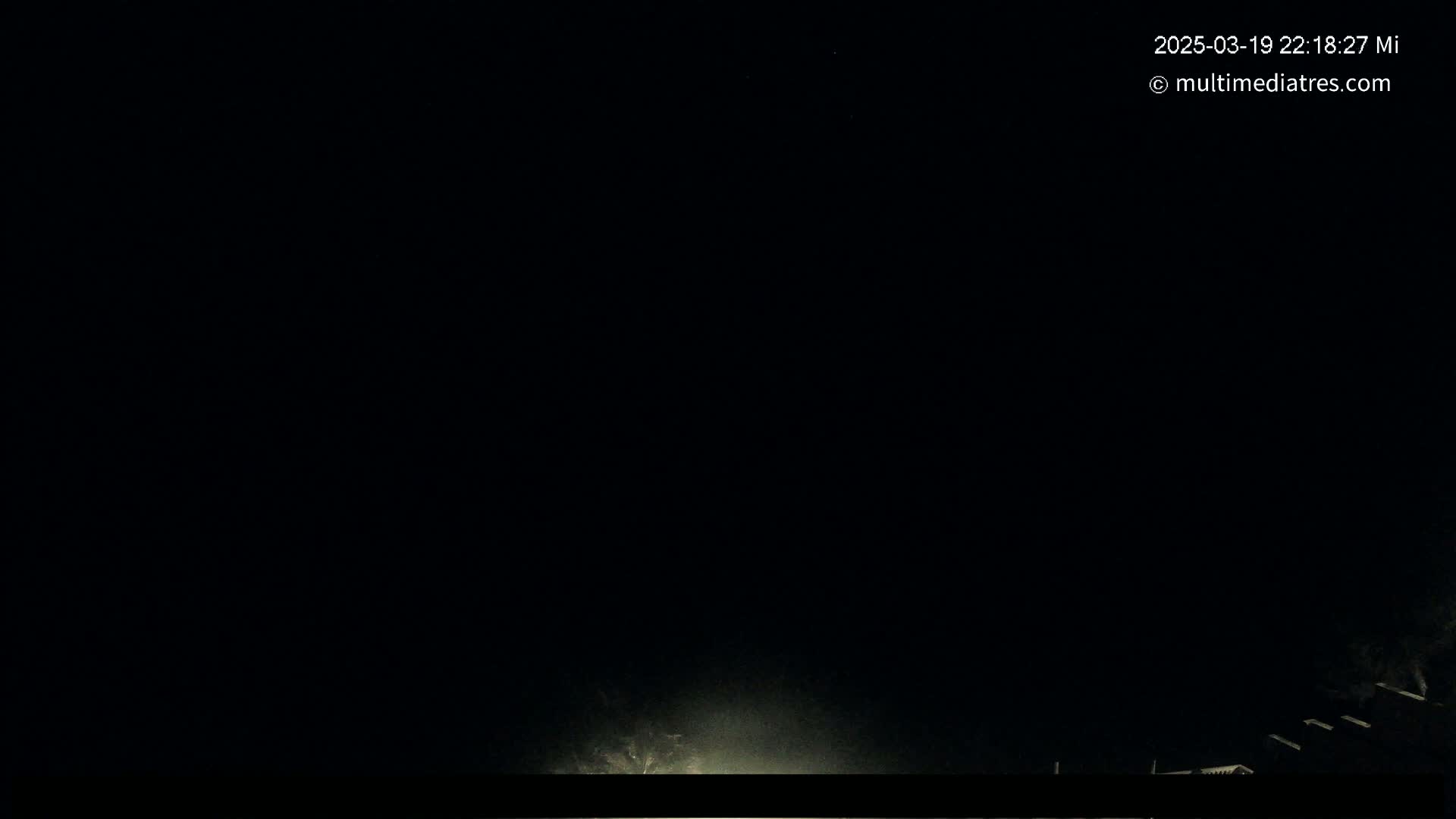 A nighttime, dark outdoor scene shows a faint light source at the bottom center, with some dark shapes possibly structures visible at the bottom right.