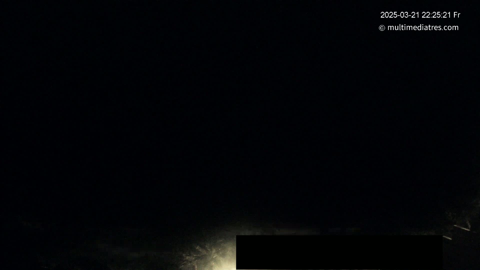 A nighttime, dark scene shows a dimly lit area, possibly a road, with a black rectangular object obscuring part of the view.