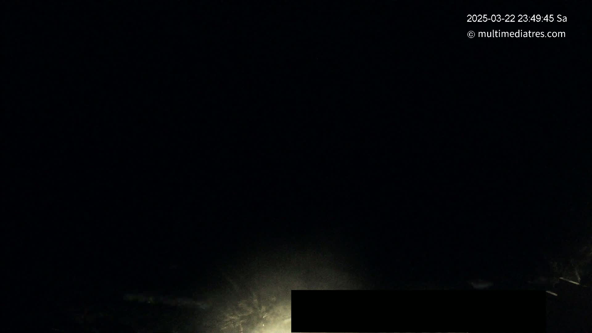 A dark, nighttime scene shows a low-light area illuminated by a bright light source in the bottom center, with some faint clouds or fog visible.