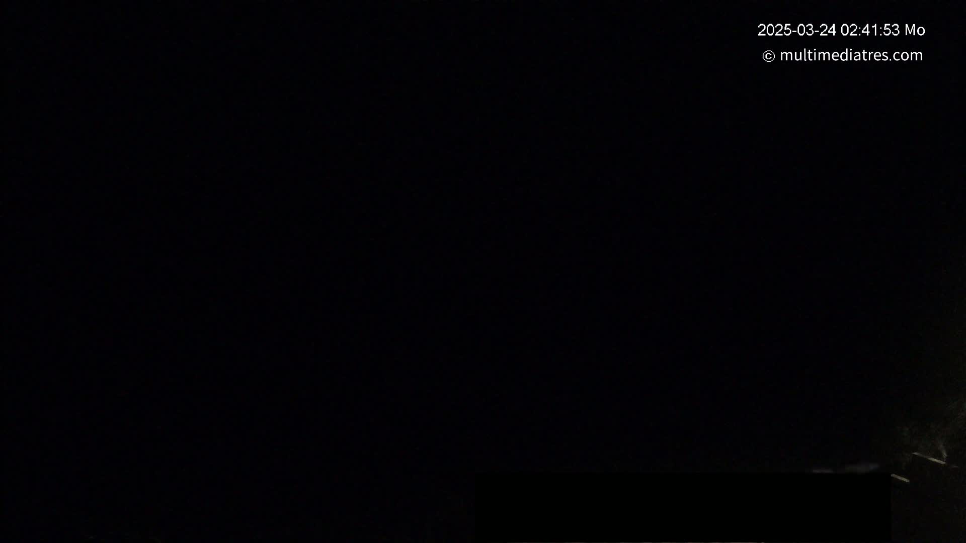 A dark, nighttime scene shows a mostly black sky with a very faint, low-lying light source near the bottom right corner.
