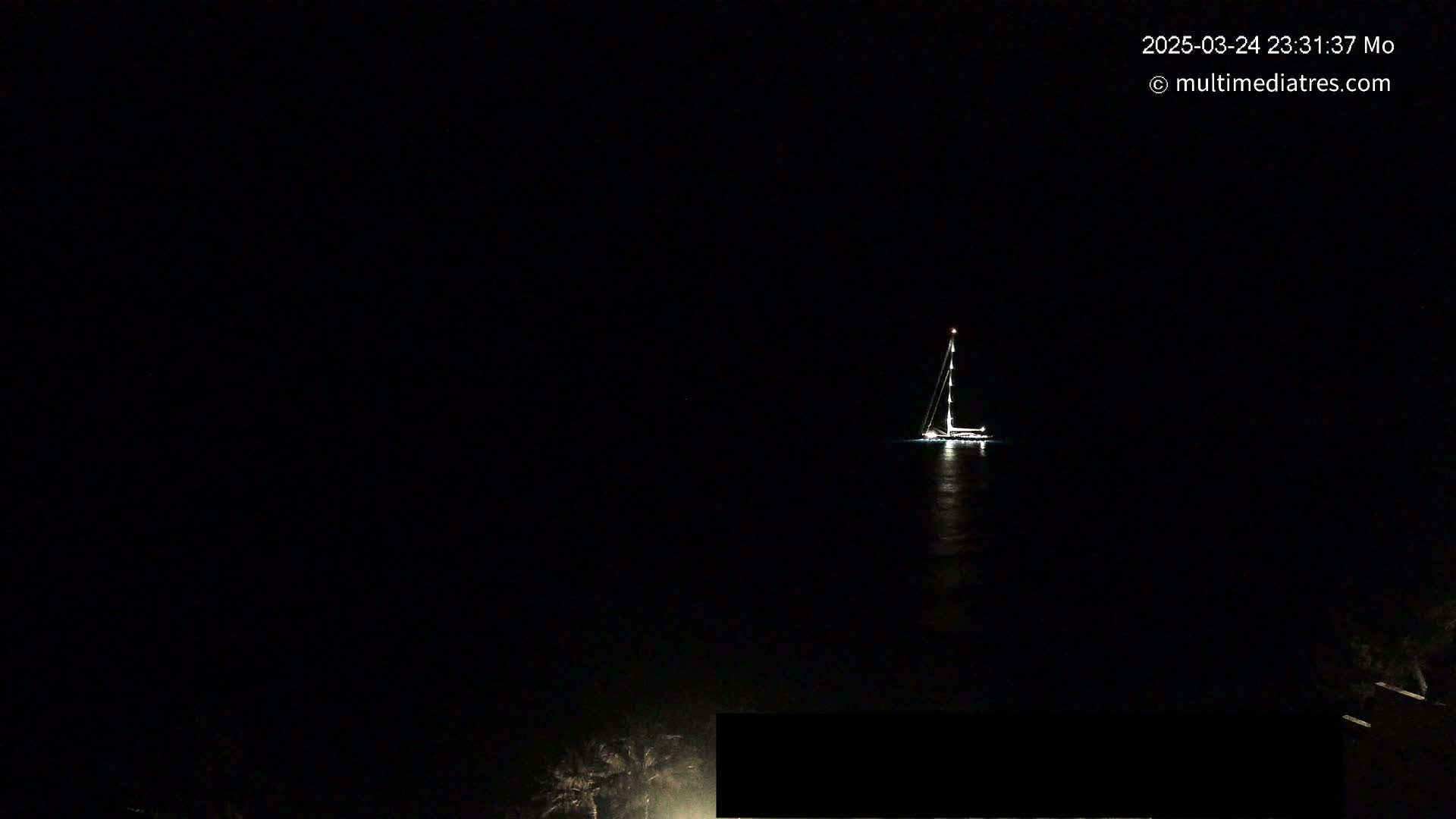 A sailboat with its lights on is visible at night on dark water.