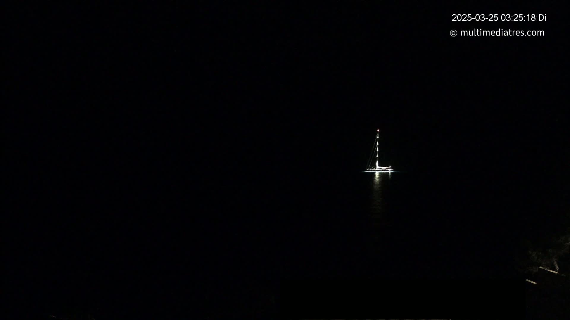 A sailboat with its lights on is visible on a dark, nighttime body of water.