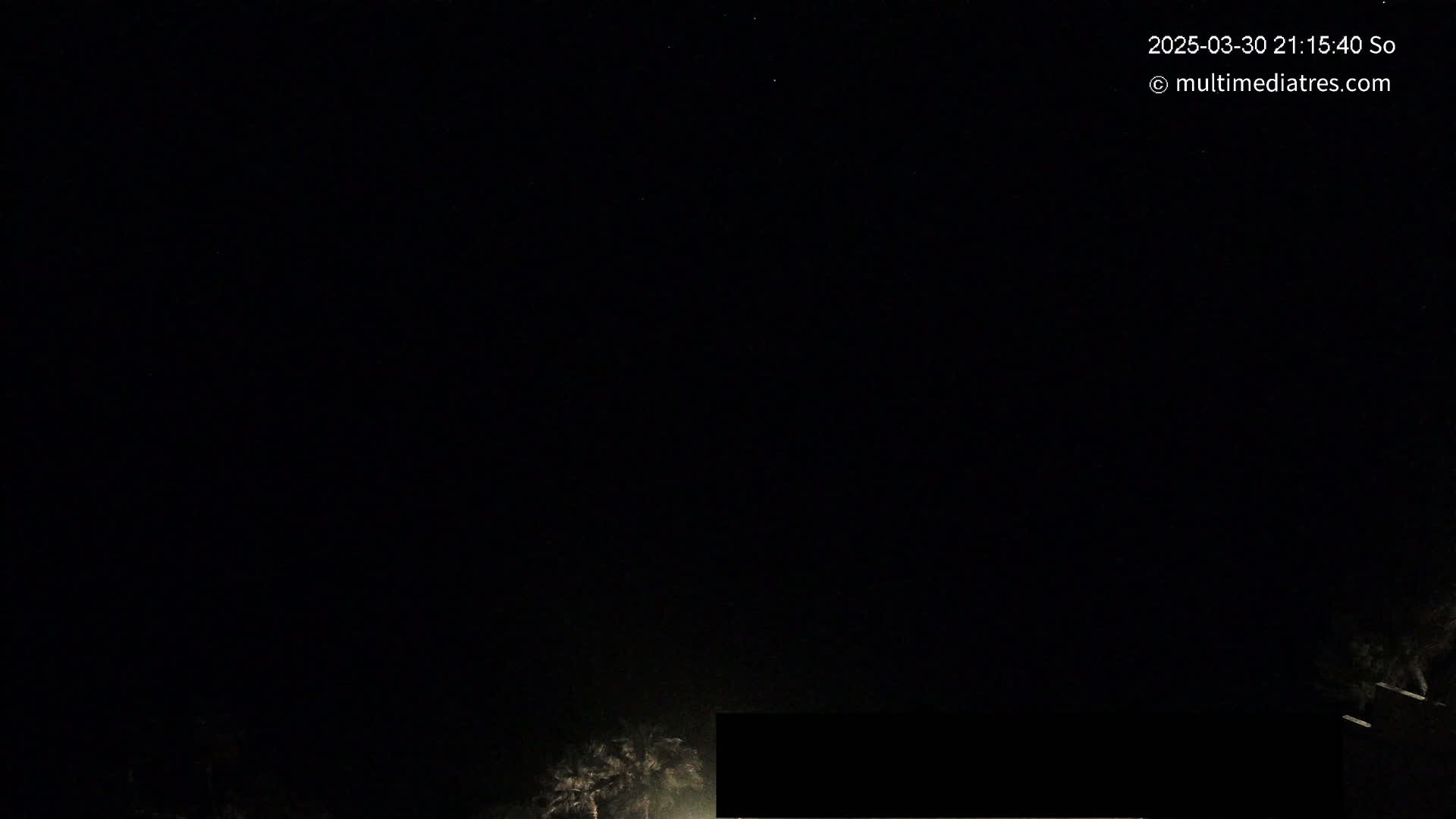 A nighttime, dark image shows a few faint lights at the bottom and a mostly clear, starlit sky.