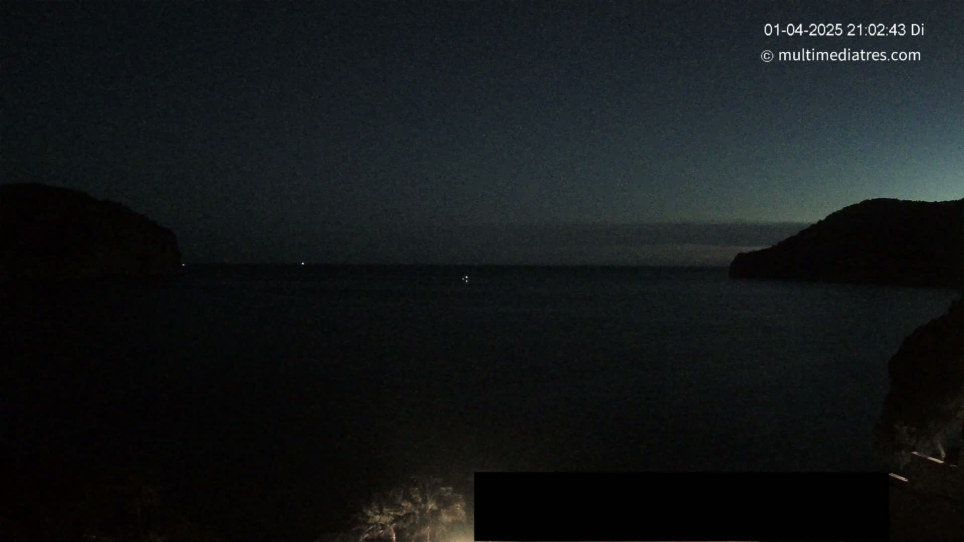 A dark, nighttime view of a calm body of water between two silhouetted hills.