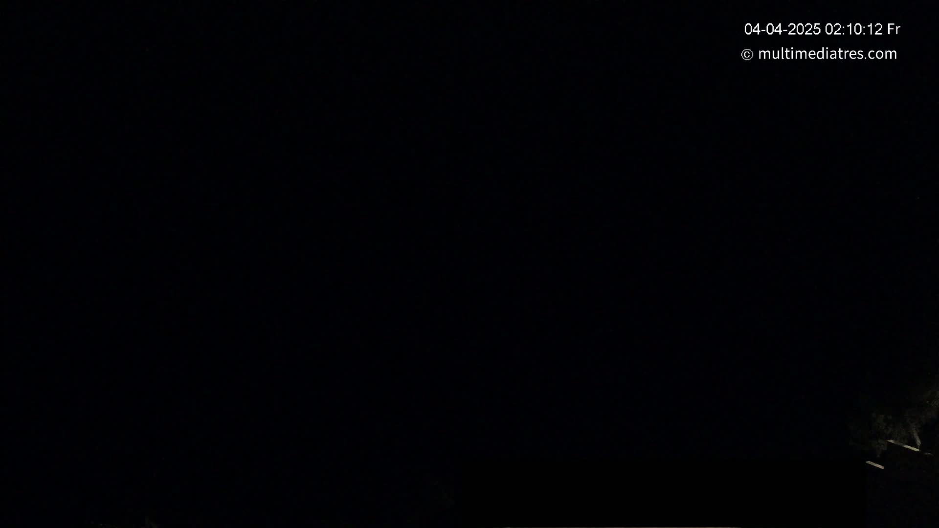 The image shows a completely black nighttime scene with a very faint, indistinct light source at the bottom right corner.