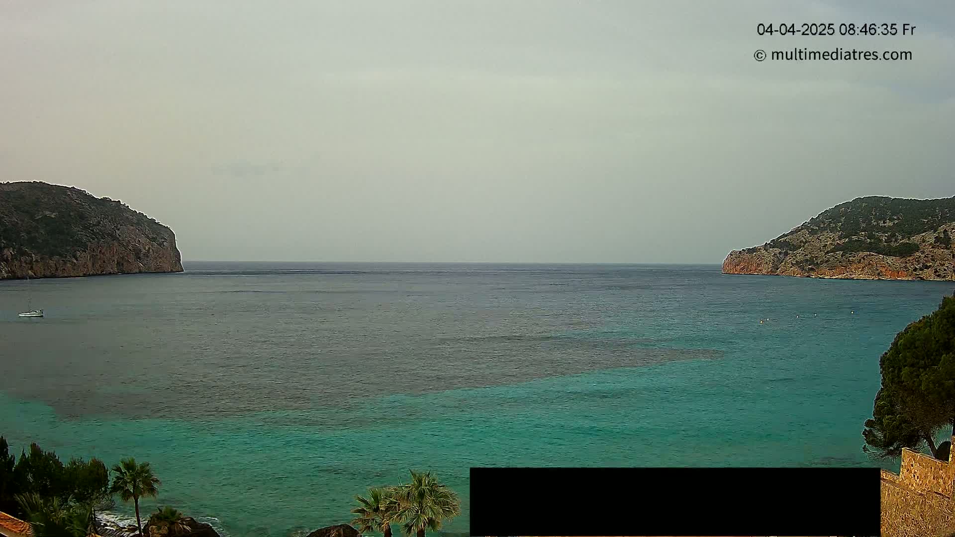 A calm, overcast day reveals a picturesque bay with teal water, two rocky headlands, and a lone boat.