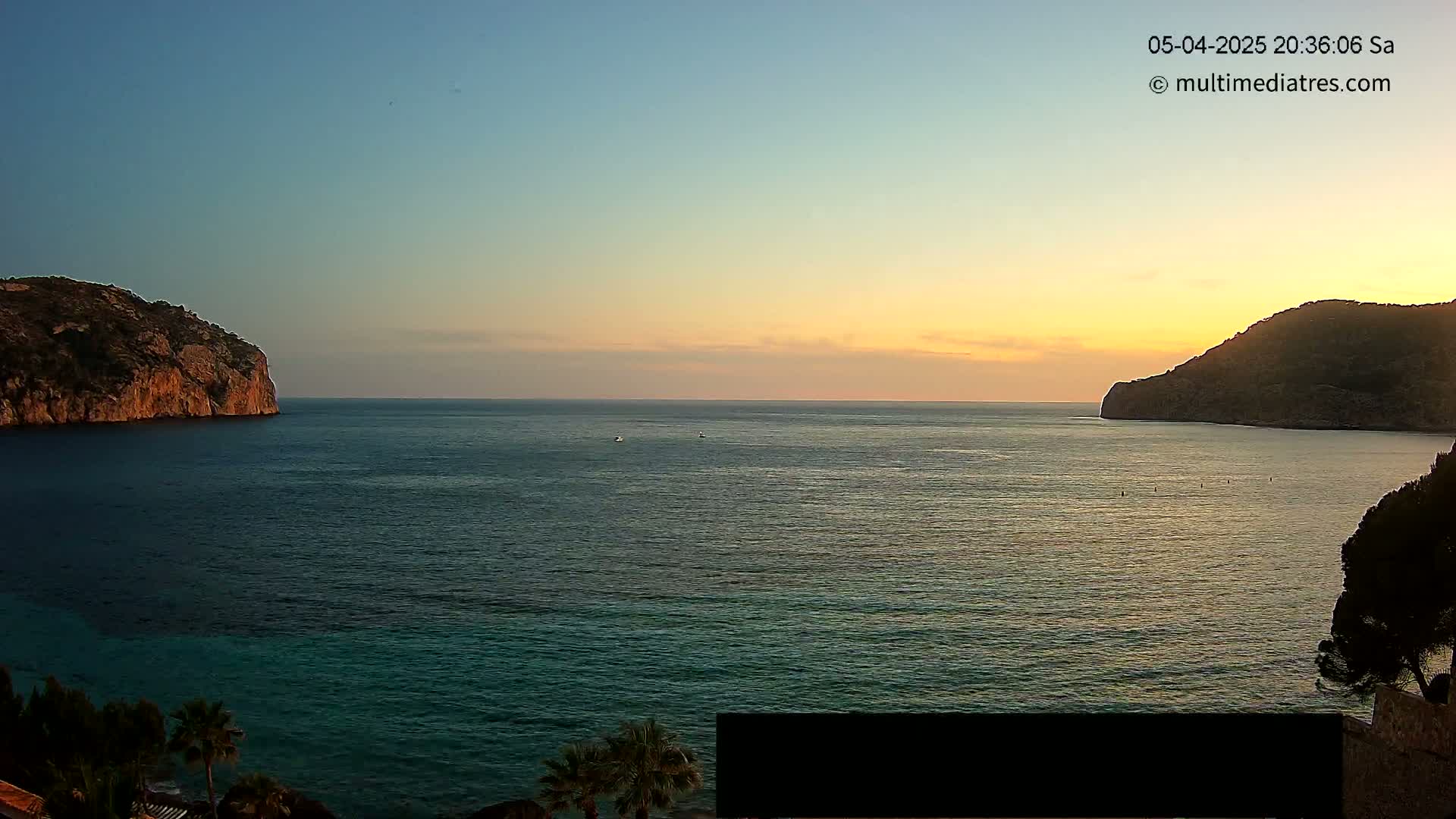 Two rocky headlands frame a calm sea at sunset.