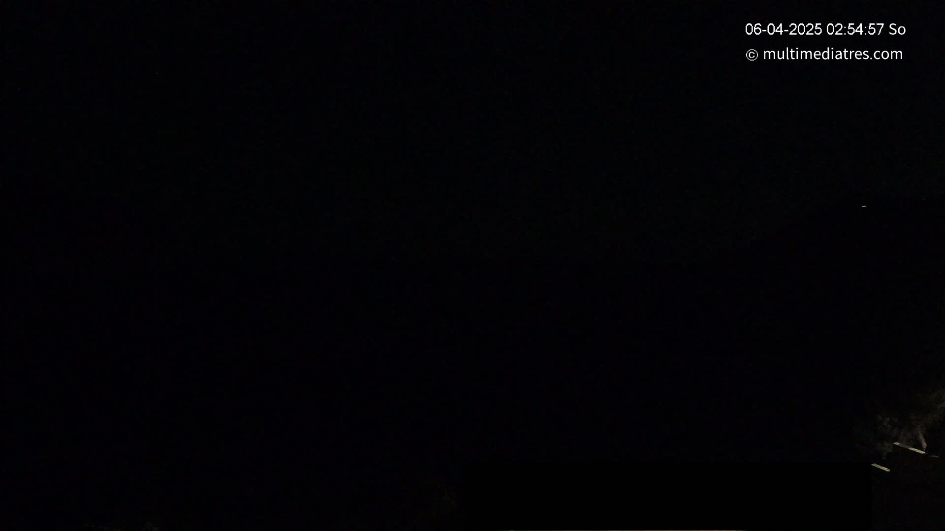A nighttime image shows a dark sky with a few faint lights in the distance and a dark, indistinct object at the bottom.