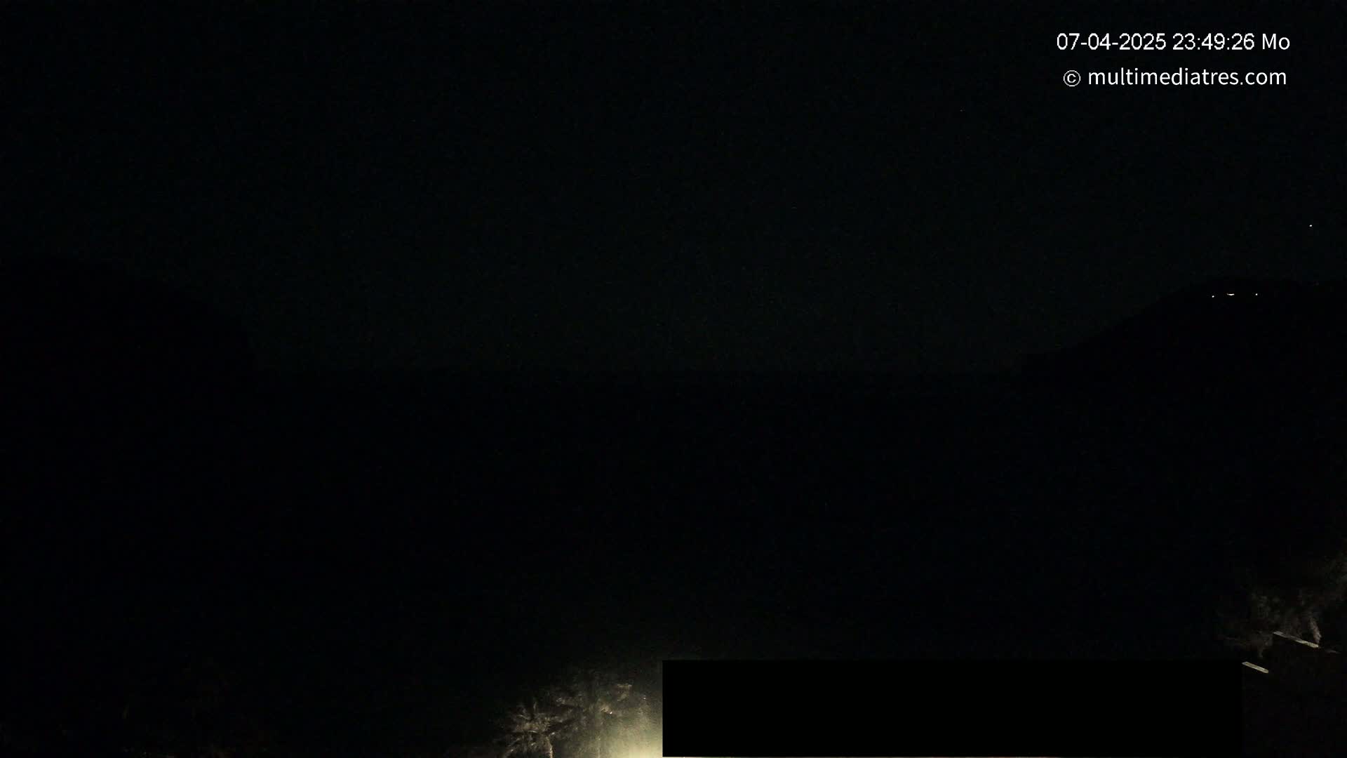 A nighttime, dark landscape is visible, with faint lights in the distance and a blurry, illuminated area in the bottom center.