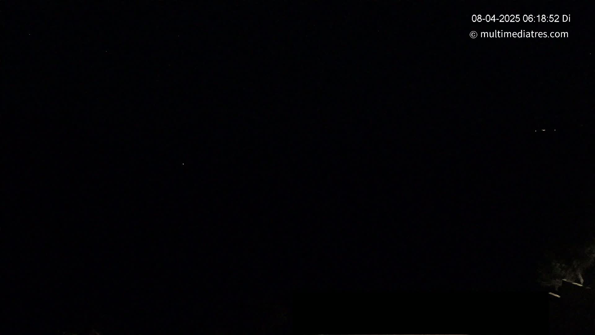 A nighttime outdoor scene shows a mostly clear, dark sky with a few faint lights visible and a dark silhouette of what appears to be a rooftop or building edge at the bottom.