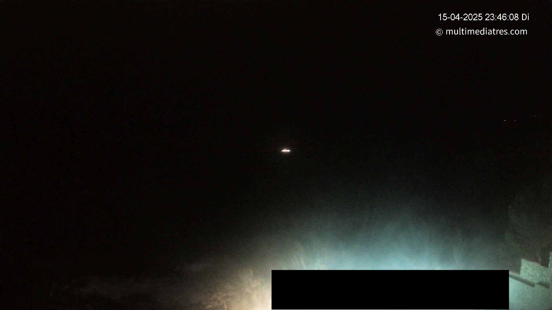 A dimly lit, nighttime scene shows a small, faint light in the distance above a dark body of water with a partially obscured object in the lower foreground.