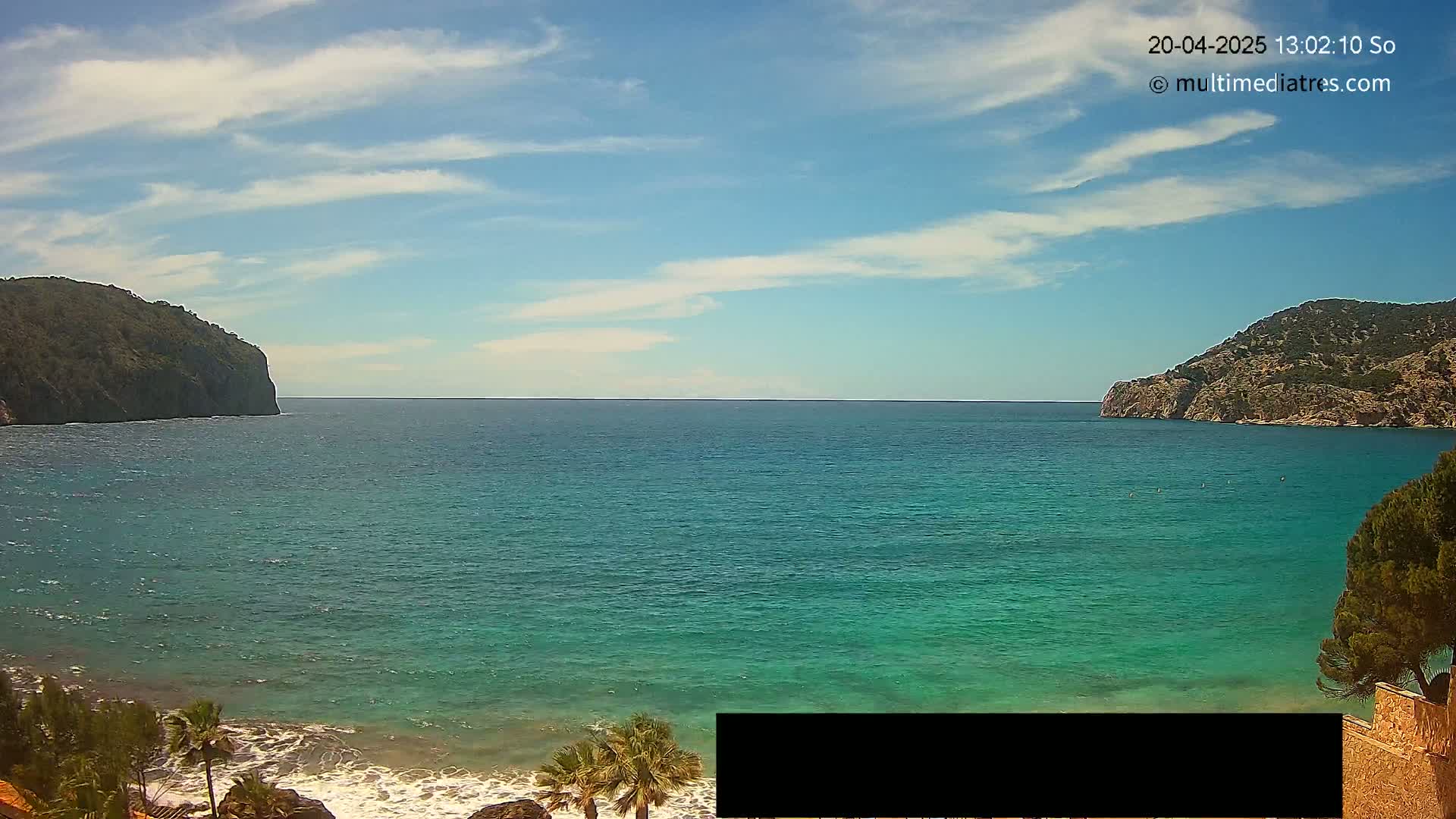 A calm, turquoise sea stretches between two rocky headlands under a mostly sunny sky with scattered clouds.