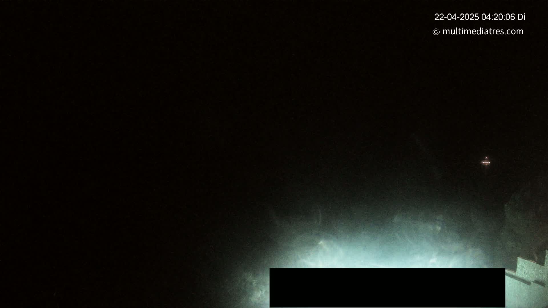 A dark, nighttime scene shows a faintly illuminated area in the lower portion of the image, with a distant light source visible in the upper portion.