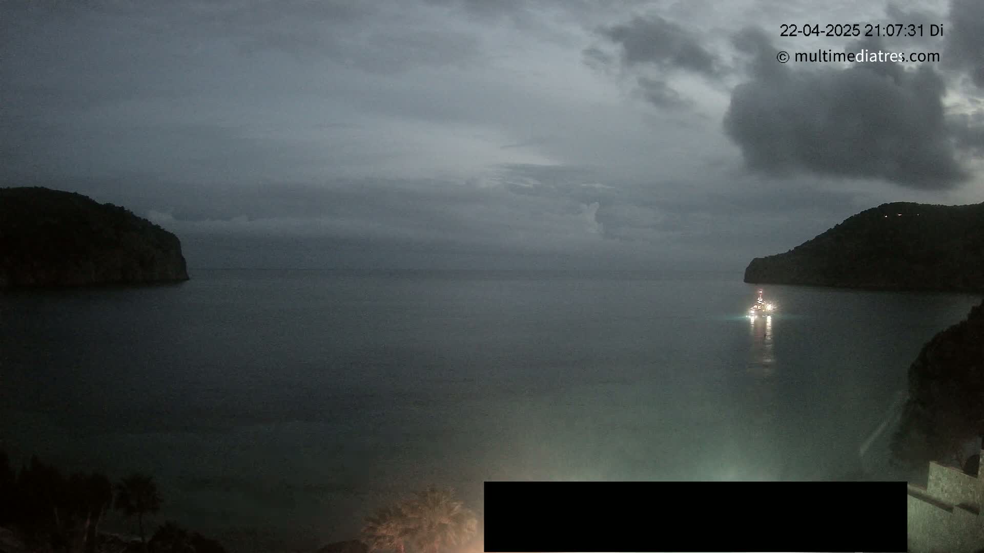 A dark, overcast sky hangs over a calm body of water between two shadowy hills, with a single boat visible in the center.