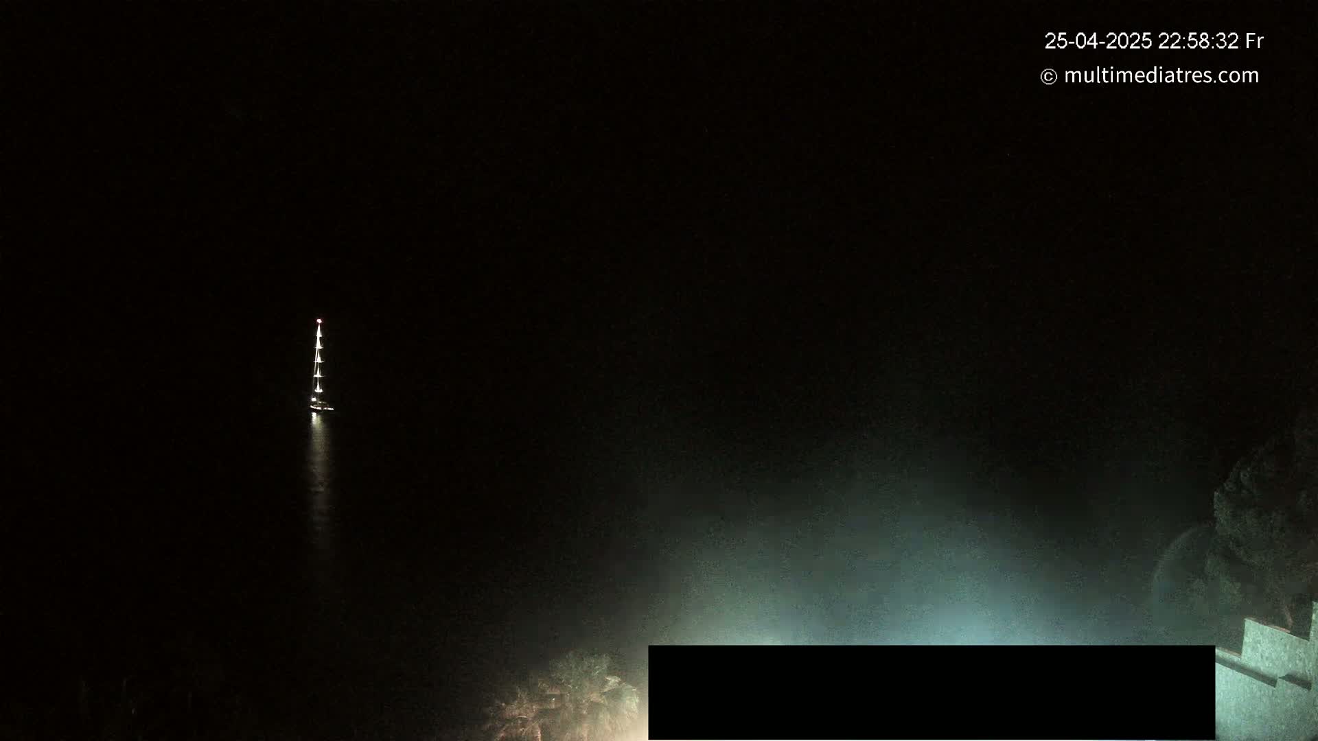 A sailboat with lights is visible on dark water at night.