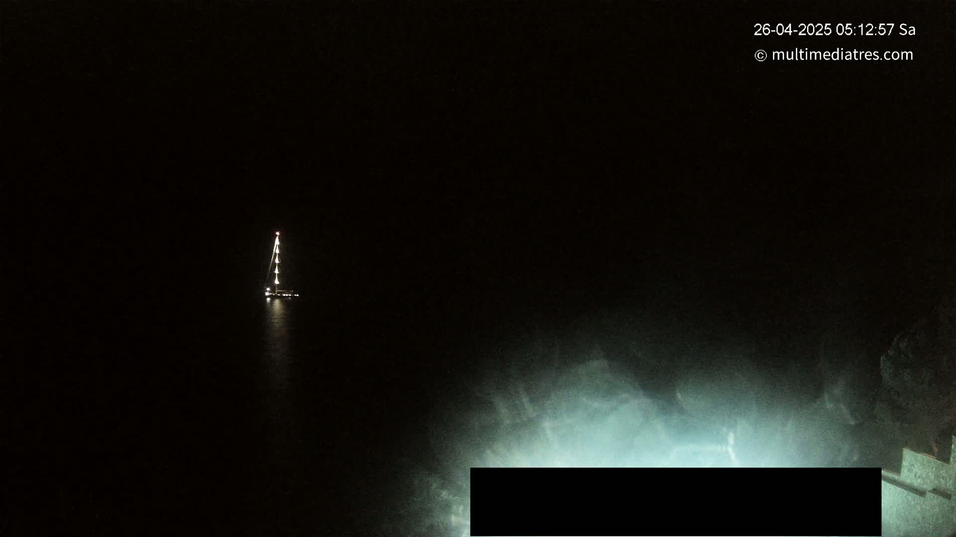 A sailboat with lights on is visible in the dark water at night.