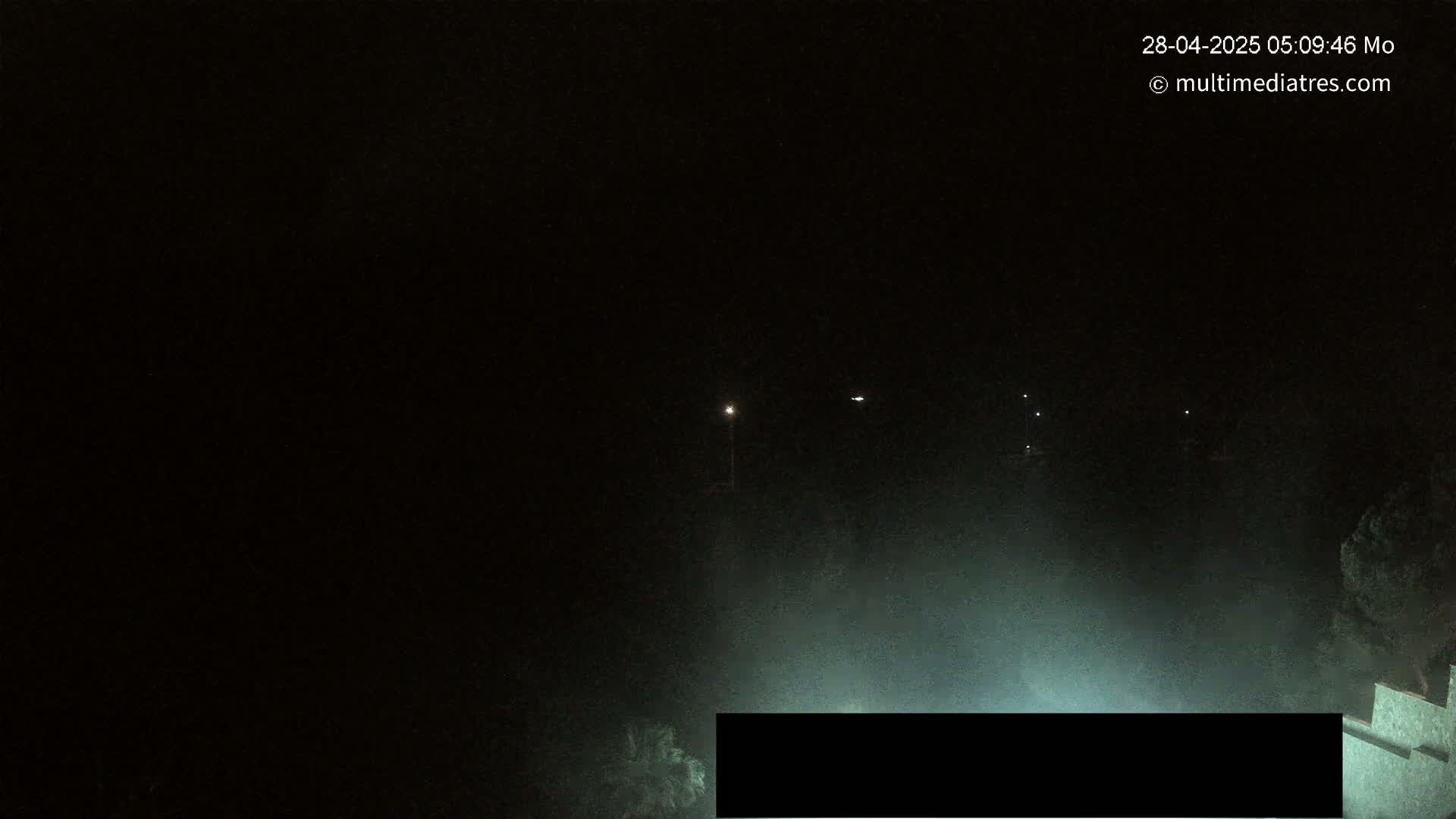 A nighttime, foggy scene shows a few distant lights and a partially visible structure in the bottom right corner.