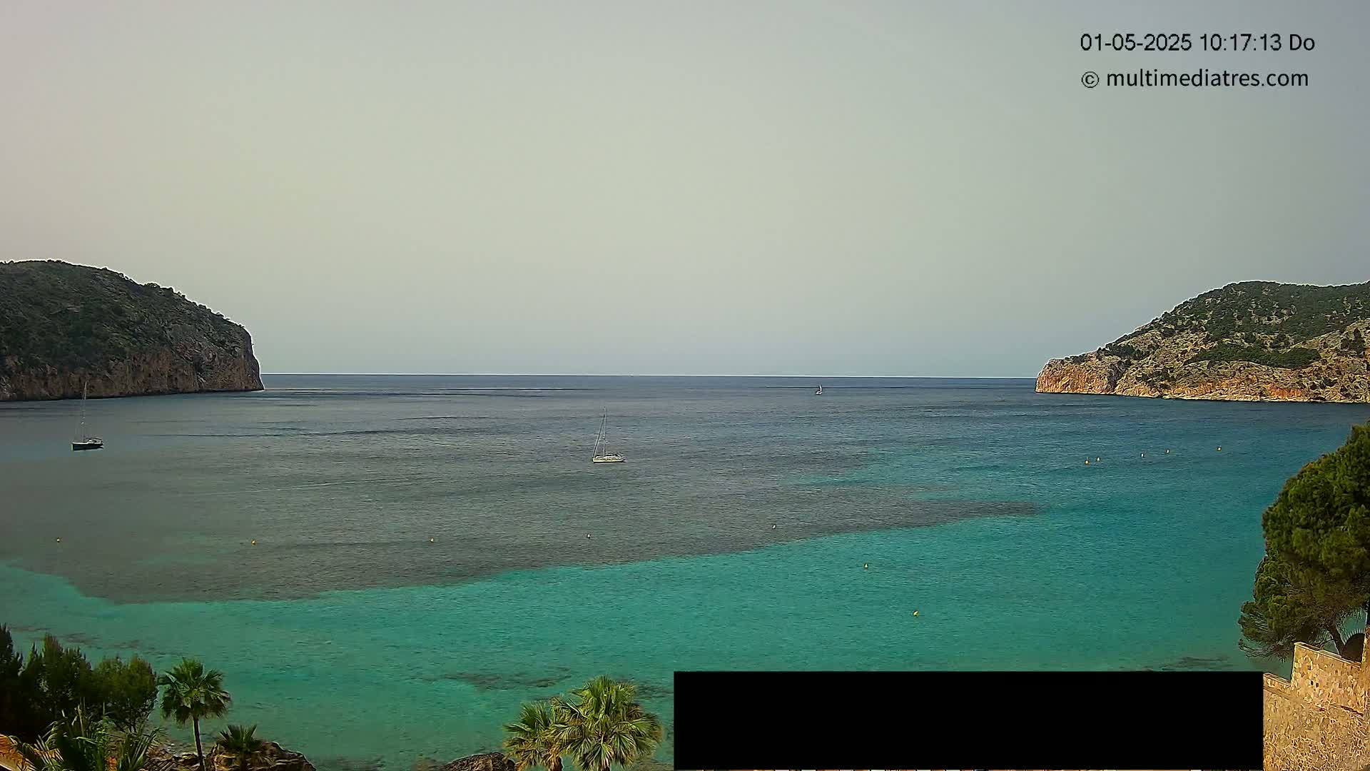 A tranquil teal bay is nestled between two verdant hills under a hazy sky.