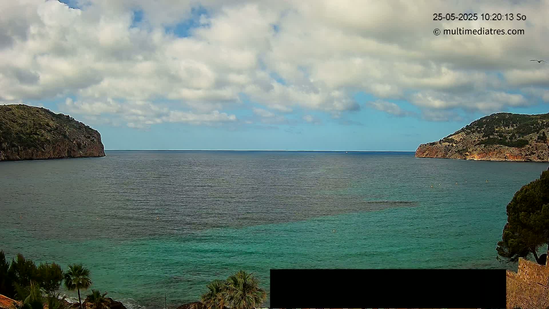A partly cloudy day reveals a tranquil cove of teal water nestled between two rocky hillsides.