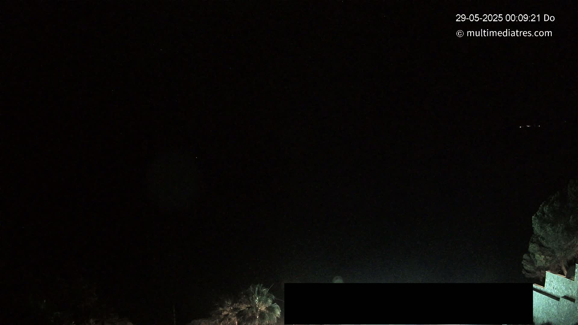 A nighttime view shows a dark sky with a few distant lights and some vegetation at the bottom of the frame.