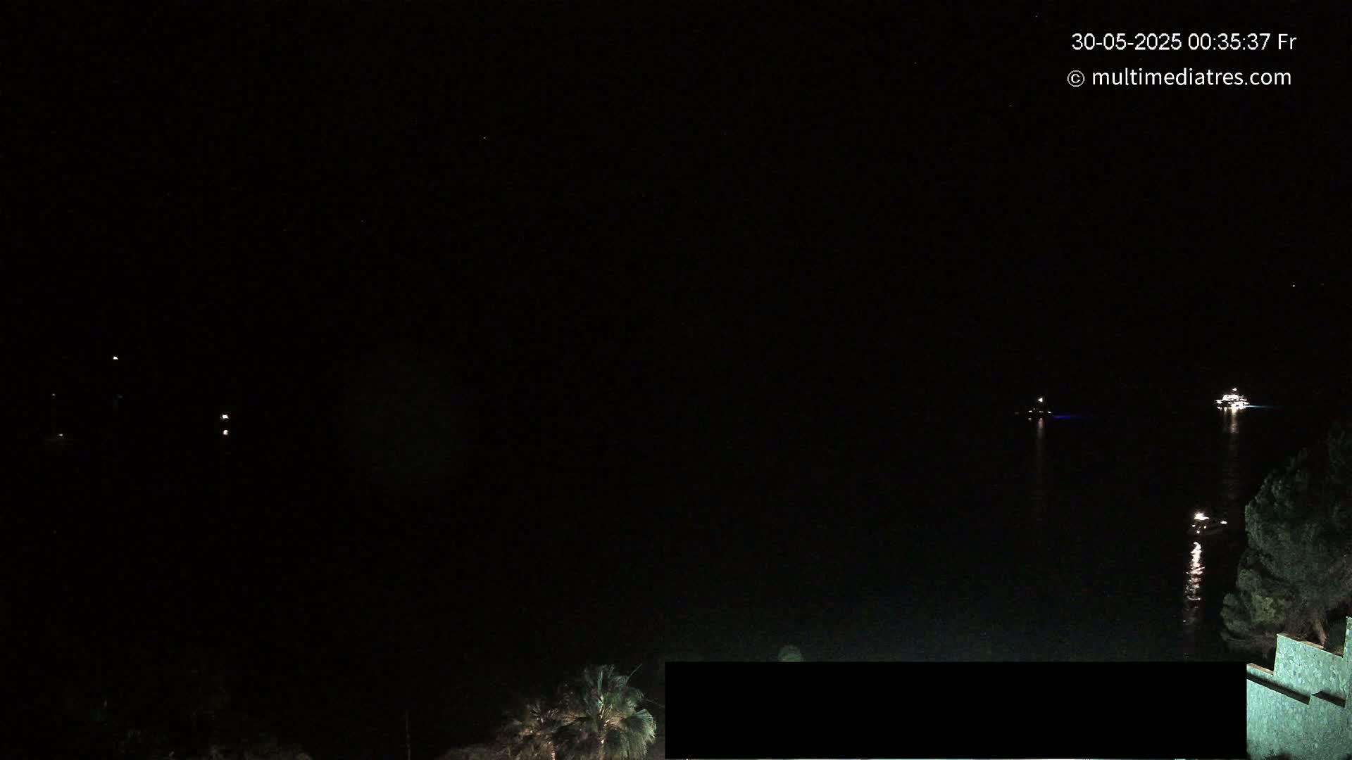 A nighttime, dark, seaside scene shows two distant boats on the water with some vegetation visible at the bottom right.