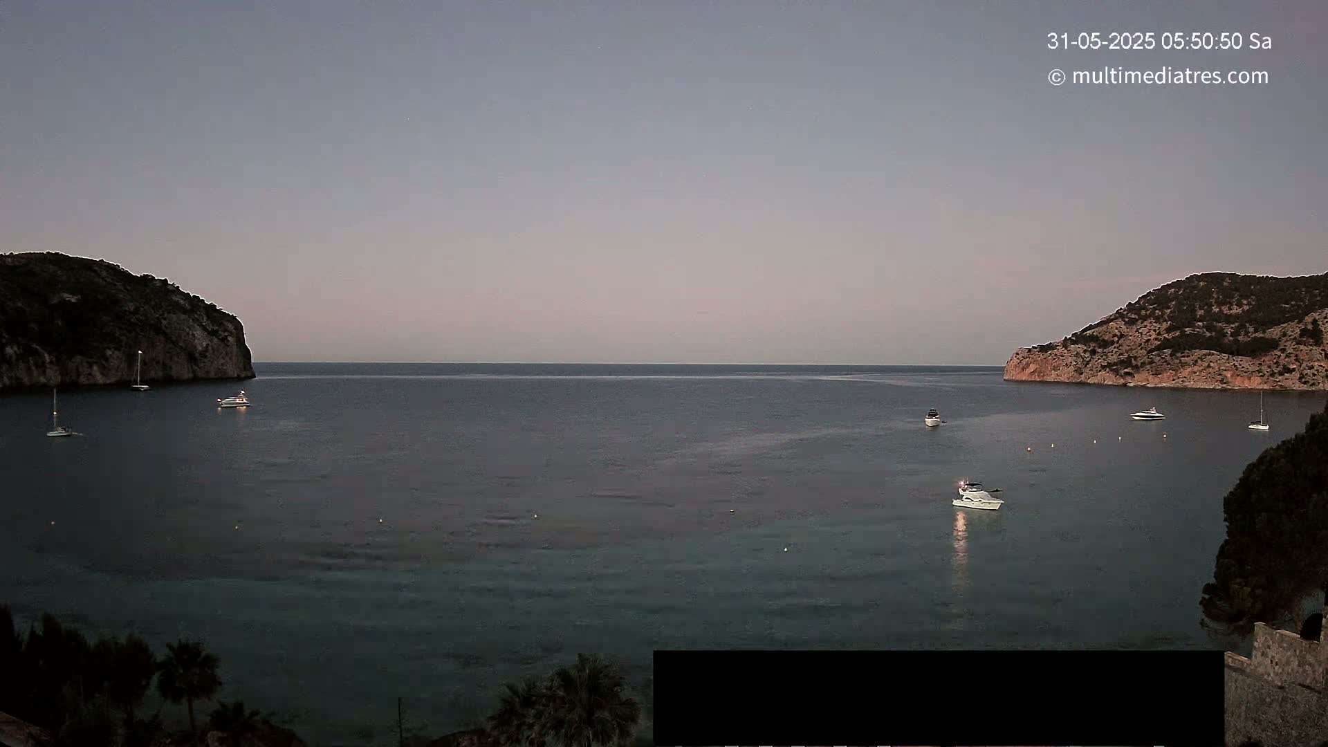 A calm, twilight sea is nestled between two dark hills, with several boats scattered across the water.