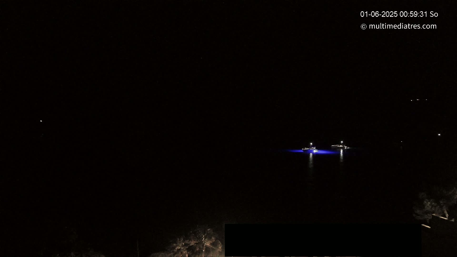At night, two boats with lights are visible on a dark body of water, under a clear, starlit sky.