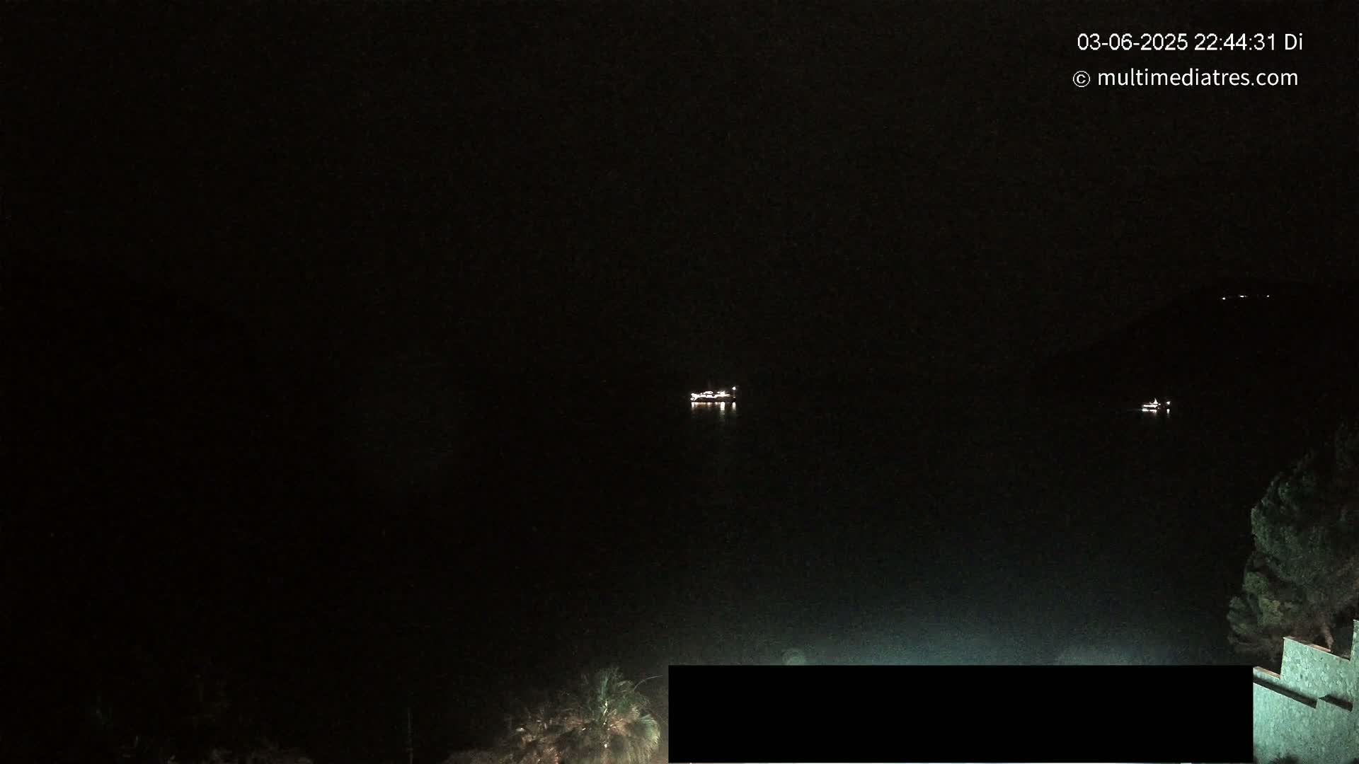 At night, two small, distant lights are visible on dark water, with dark land and vegetation in the foreground.