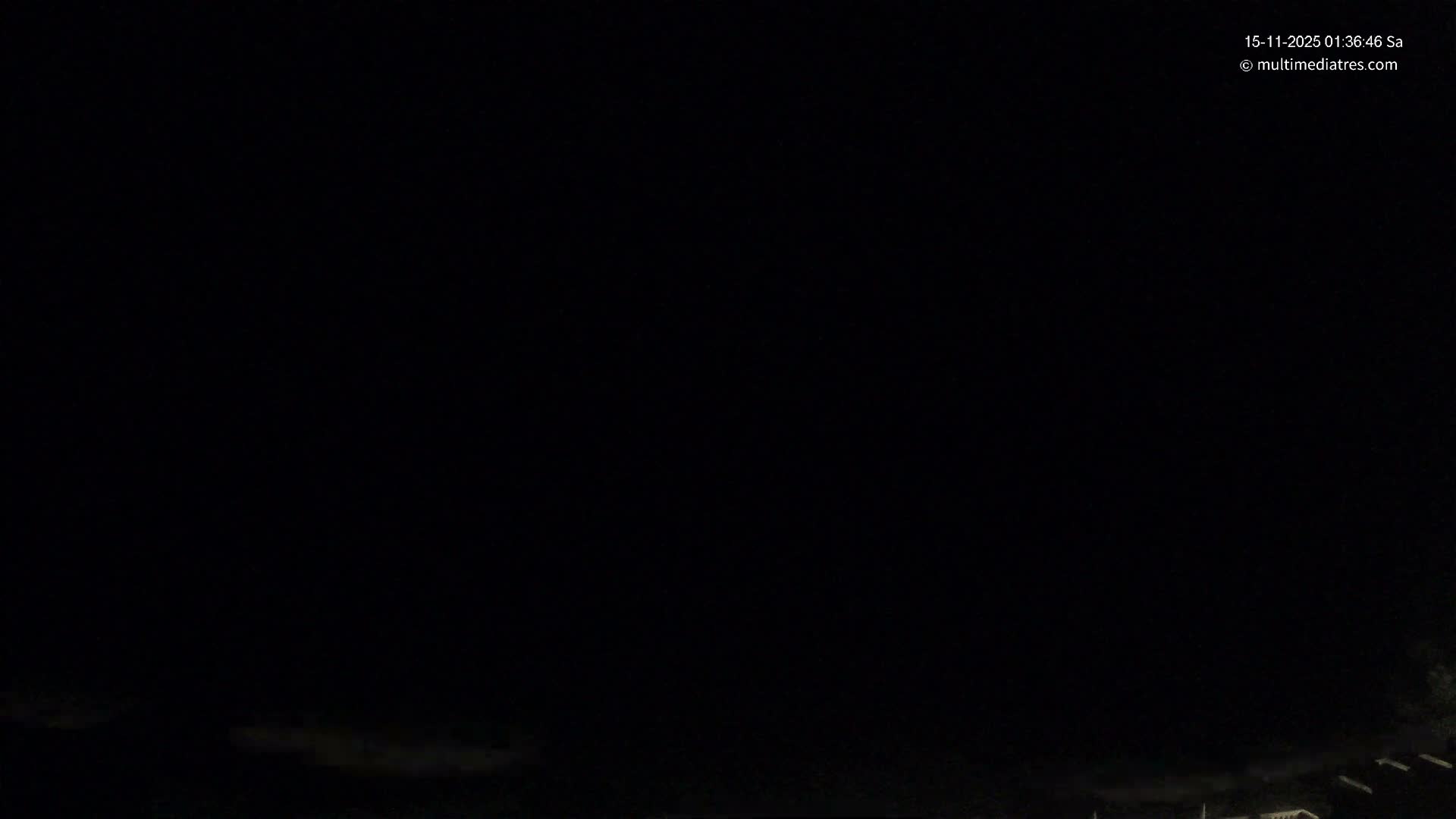 A very dark outdoor scene at night shows only faint, indistinct outlines of distant land or structures at the bottom under what appears to be an overcast sky.