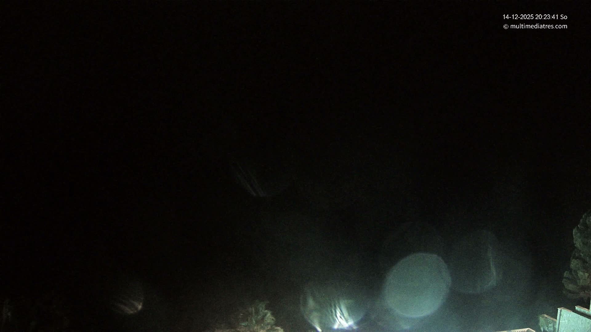 A beautiful bay with turquoise water and gentle waves is framed by rocky, vegetated cliffs on either side, all bathed in sunlight under a clear blue sky dotted with fluffy white clouds.