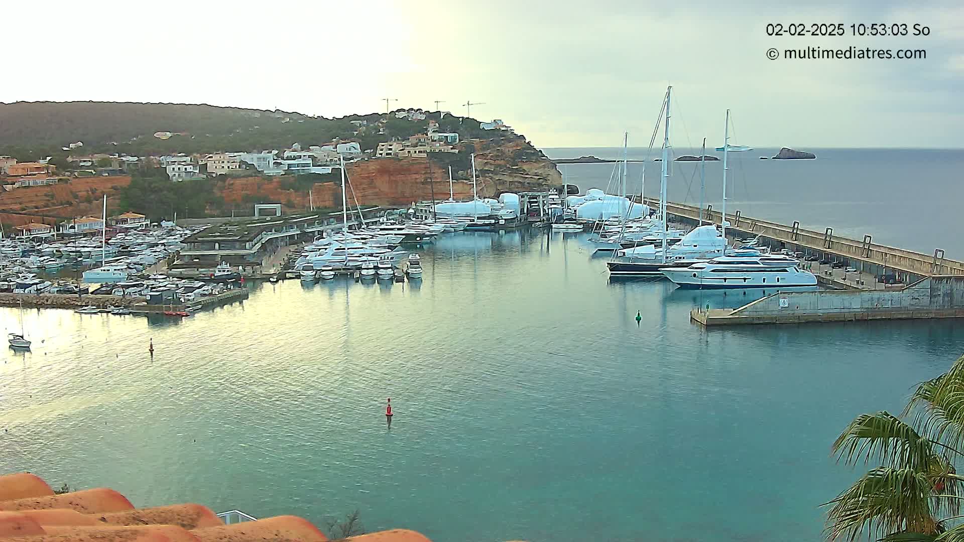A marina filled with numerous yachts and boats is situated beside a cliffside town under an overcast sky.
