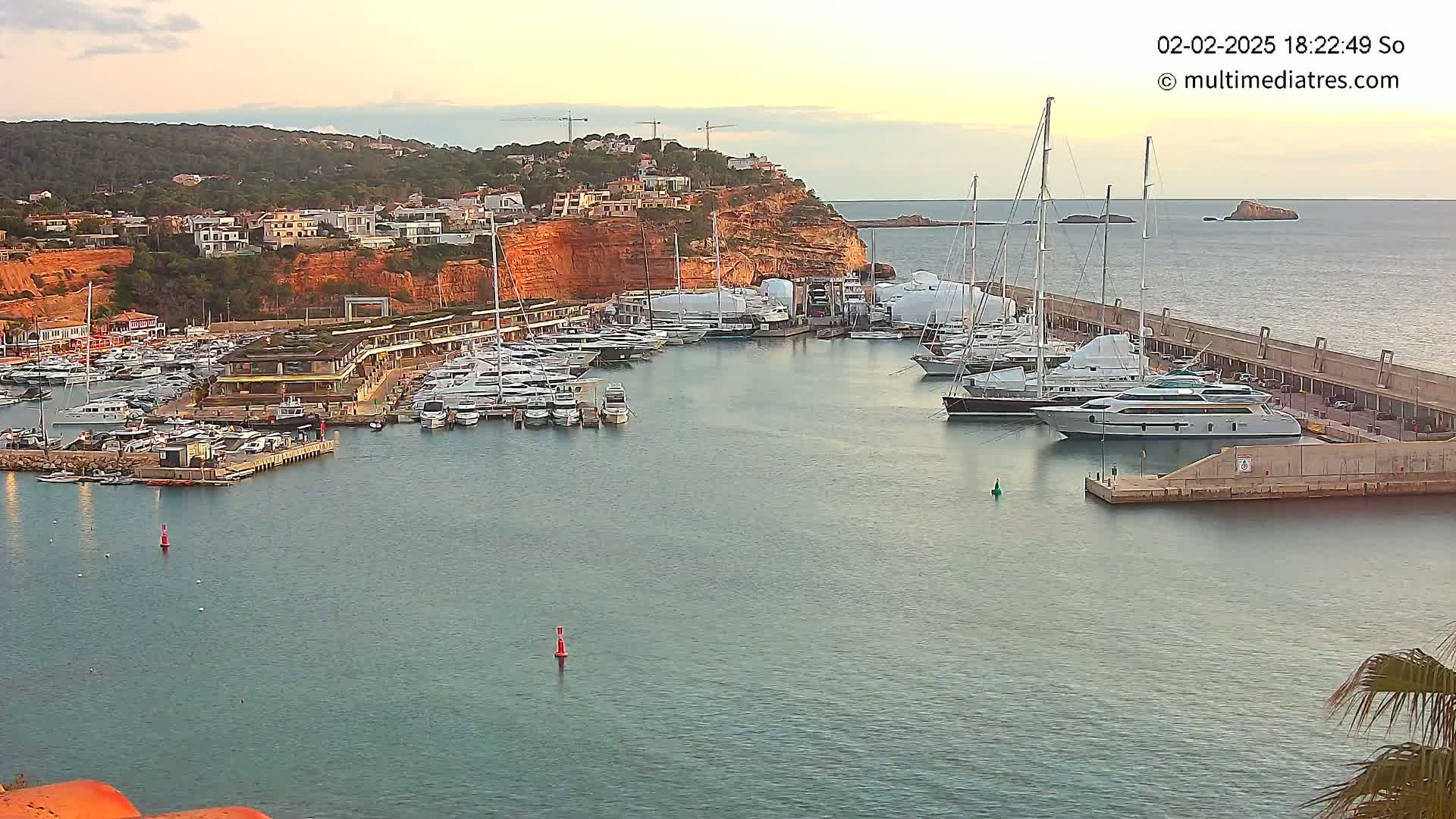 A calm harbor filled with numerous yachts and boats is nestled against a hillside of buildings under a twilight sky.