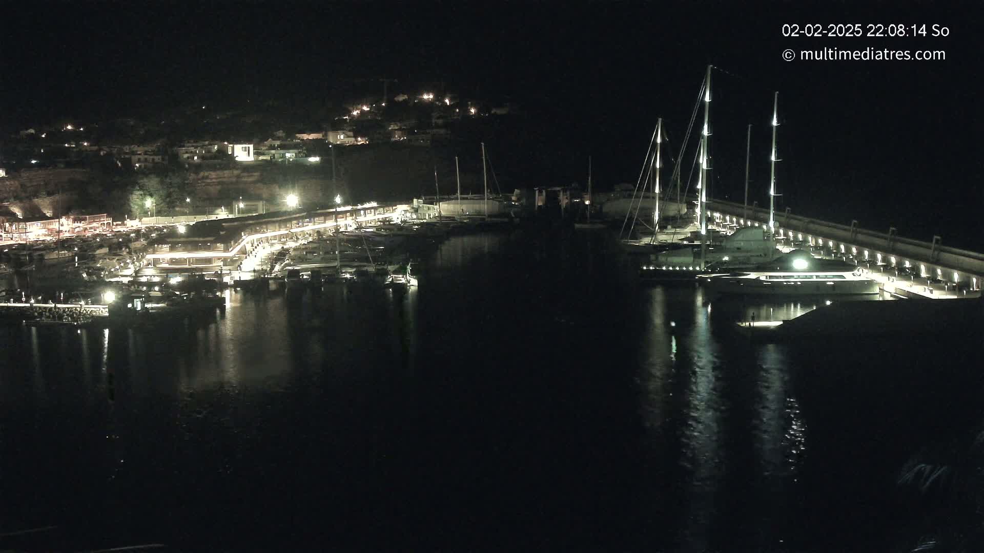 A nighttime view of a marina filled with boats, lit up against a dark hillside.