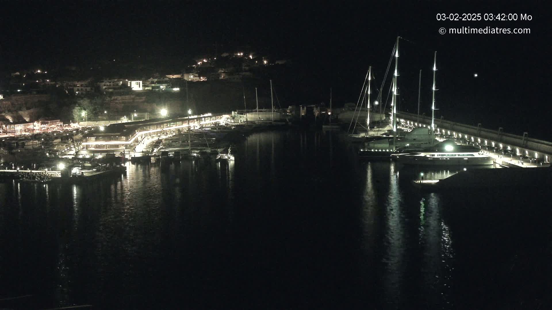 A nighttime harbor scene shows a marina filled with boats, with lights illuminating the docks and surrounding buildings.