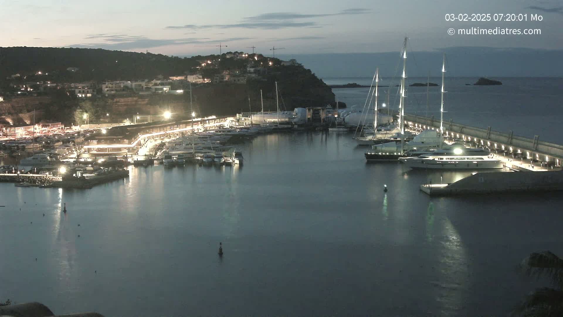 A marina filled with boats is illuminated at night under a twilight sky.