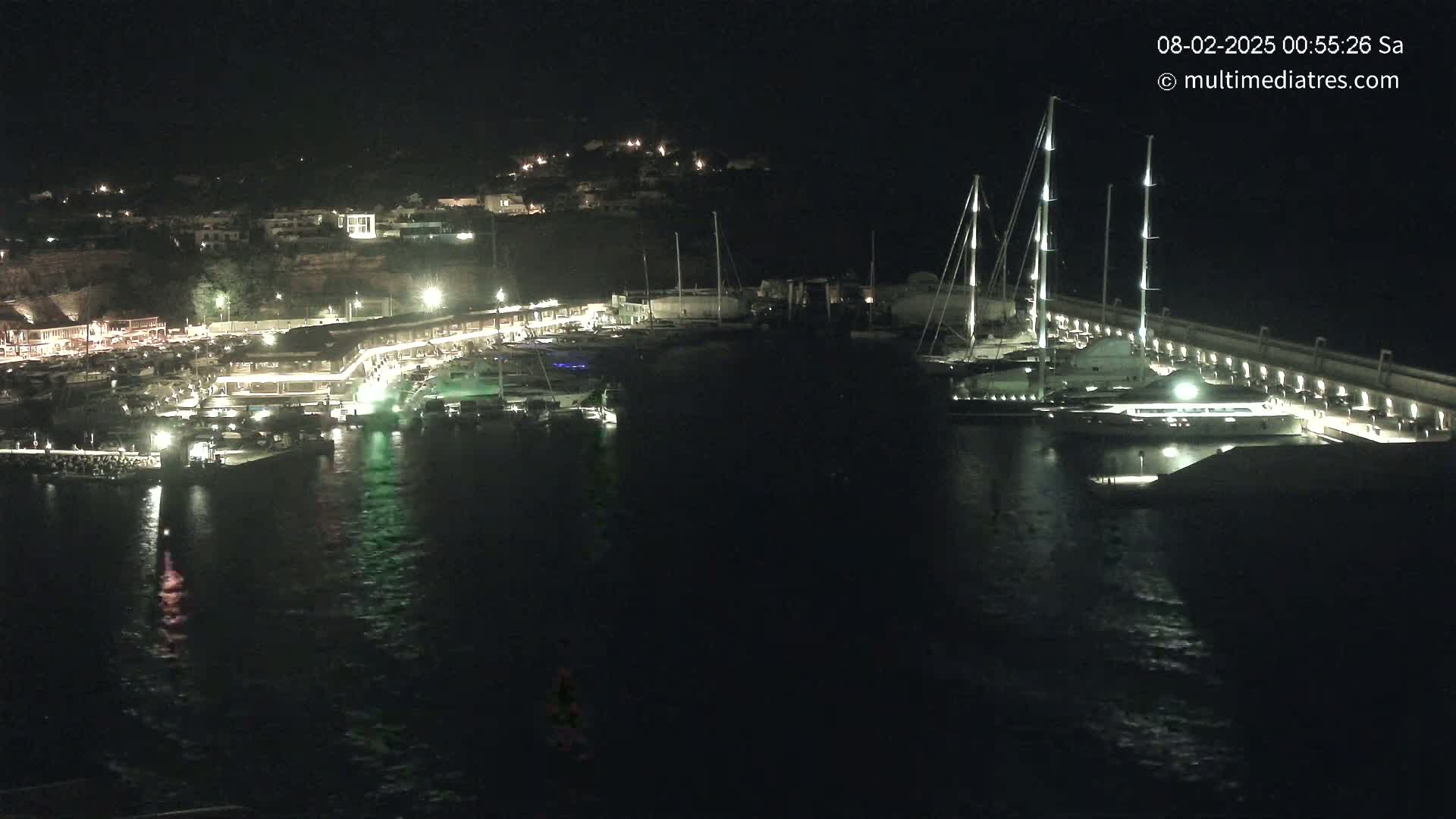 A nighttime view of a marina filled with boats, illuminated buildings, and calm dark water.