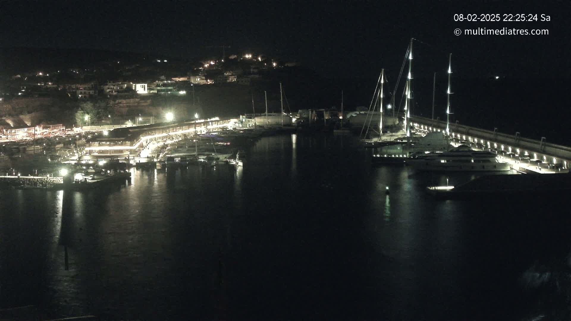 A marina at night, filled with boats and illuminated by lights along the docks and buildings on the shore.