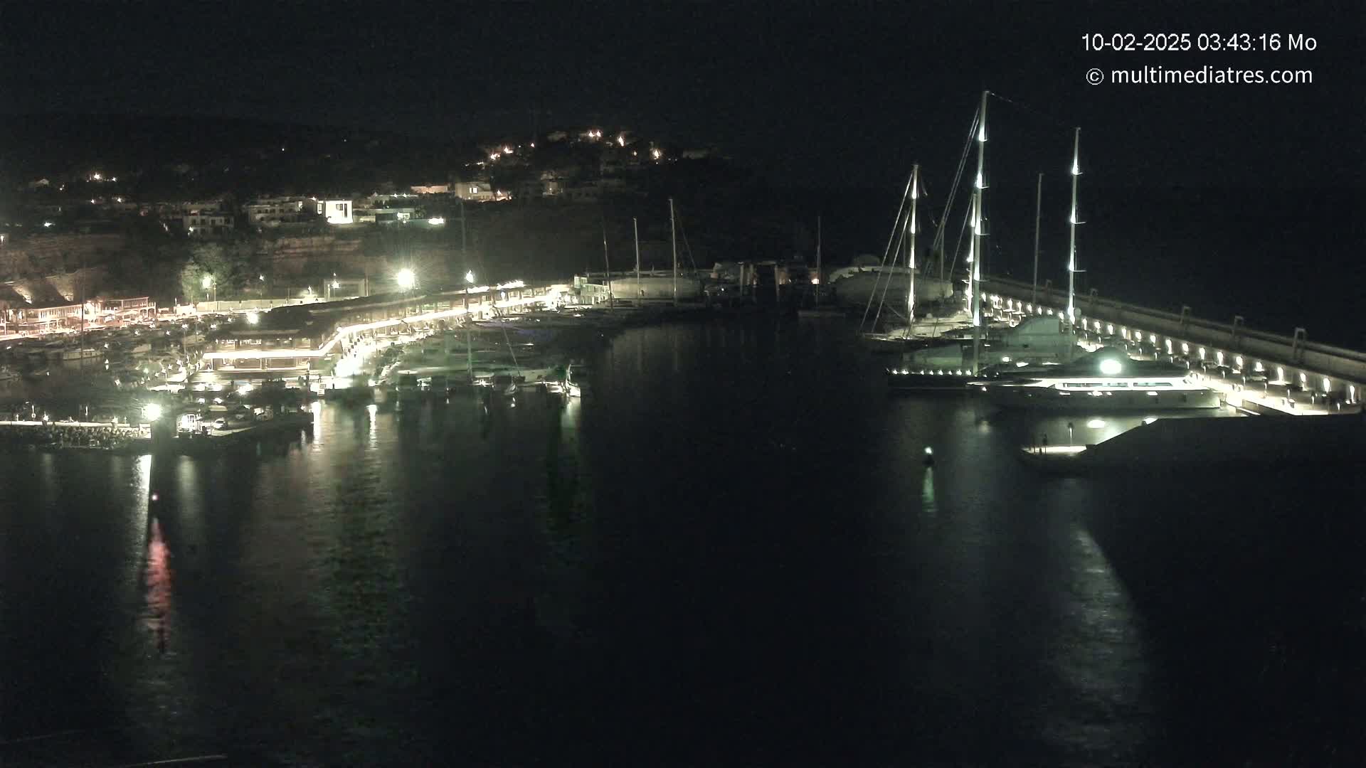A nighttime harbor scene shows numerous boats moored alongside a lit waterfront, with a large yacht prominently featured in the foreground.