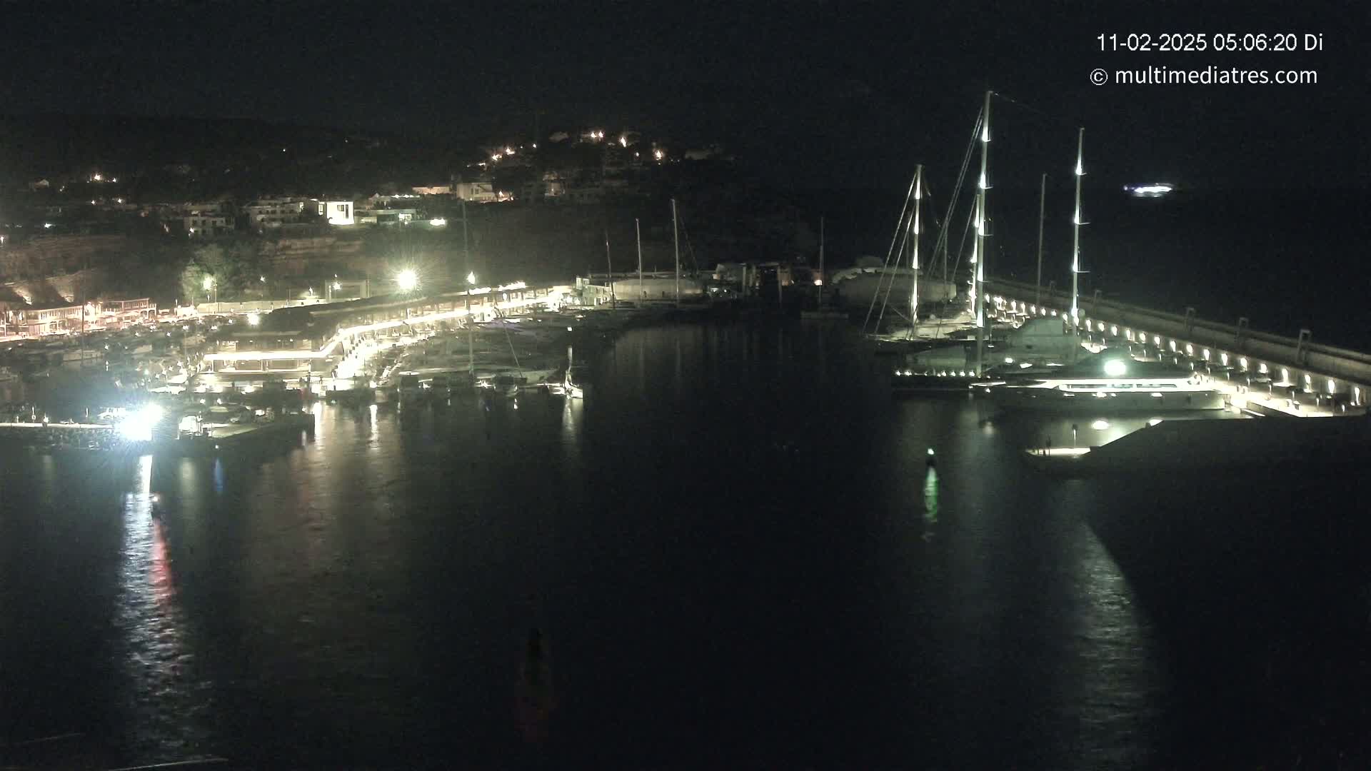 A nighttime view of a harbor filled with boats, illuminated by lights along the docks and buildings on the shore.
