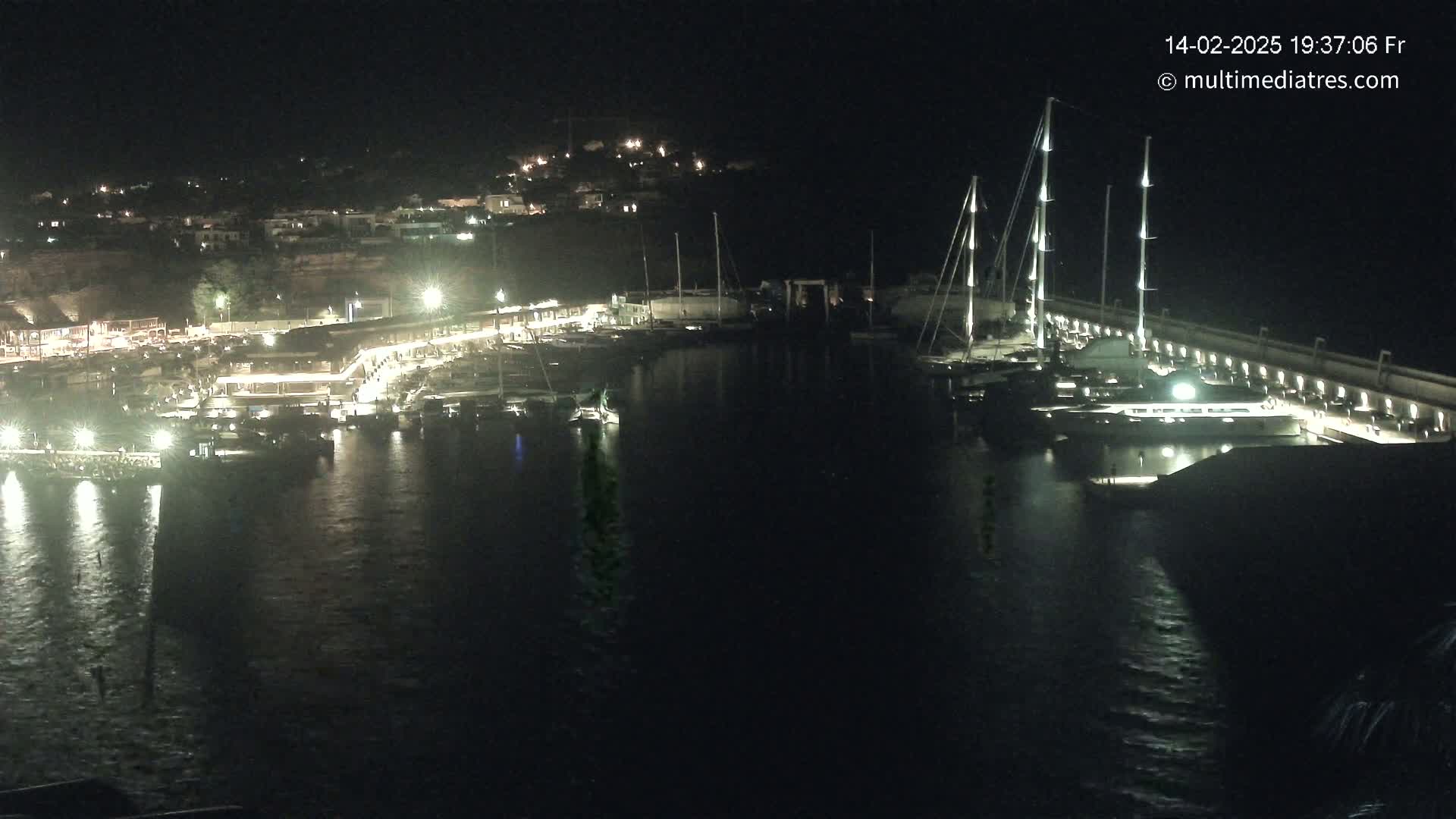 A nighttime view of a marina filled with boats, illuminated by lights along the docks and buildings on the shore.
