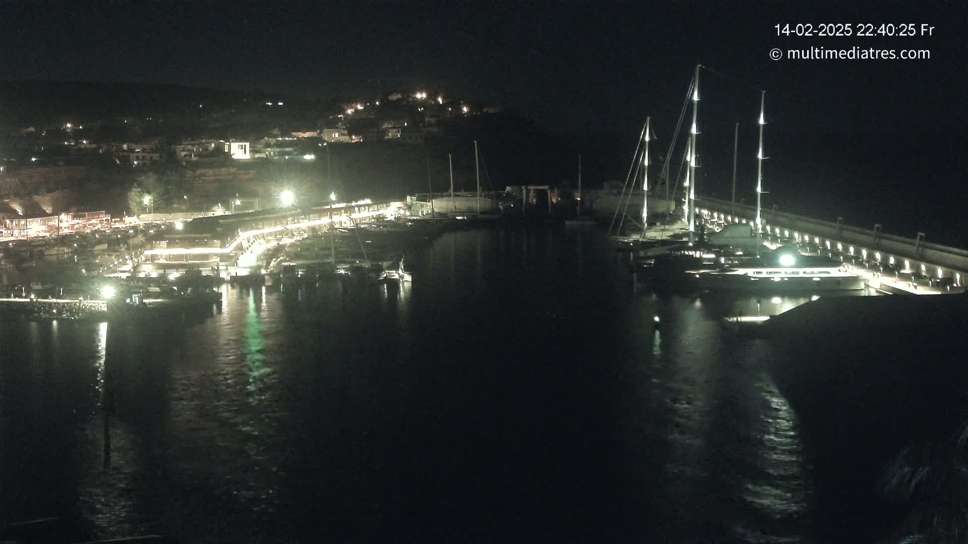 A nighttime view of a marina with numerous boats docked, illuminated by artificial lights, under a clear, dark sky.